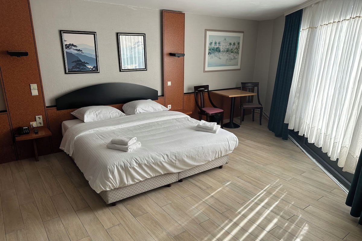 A hotel room with a large bed, a desk, two chairs, and artwork on the walls.