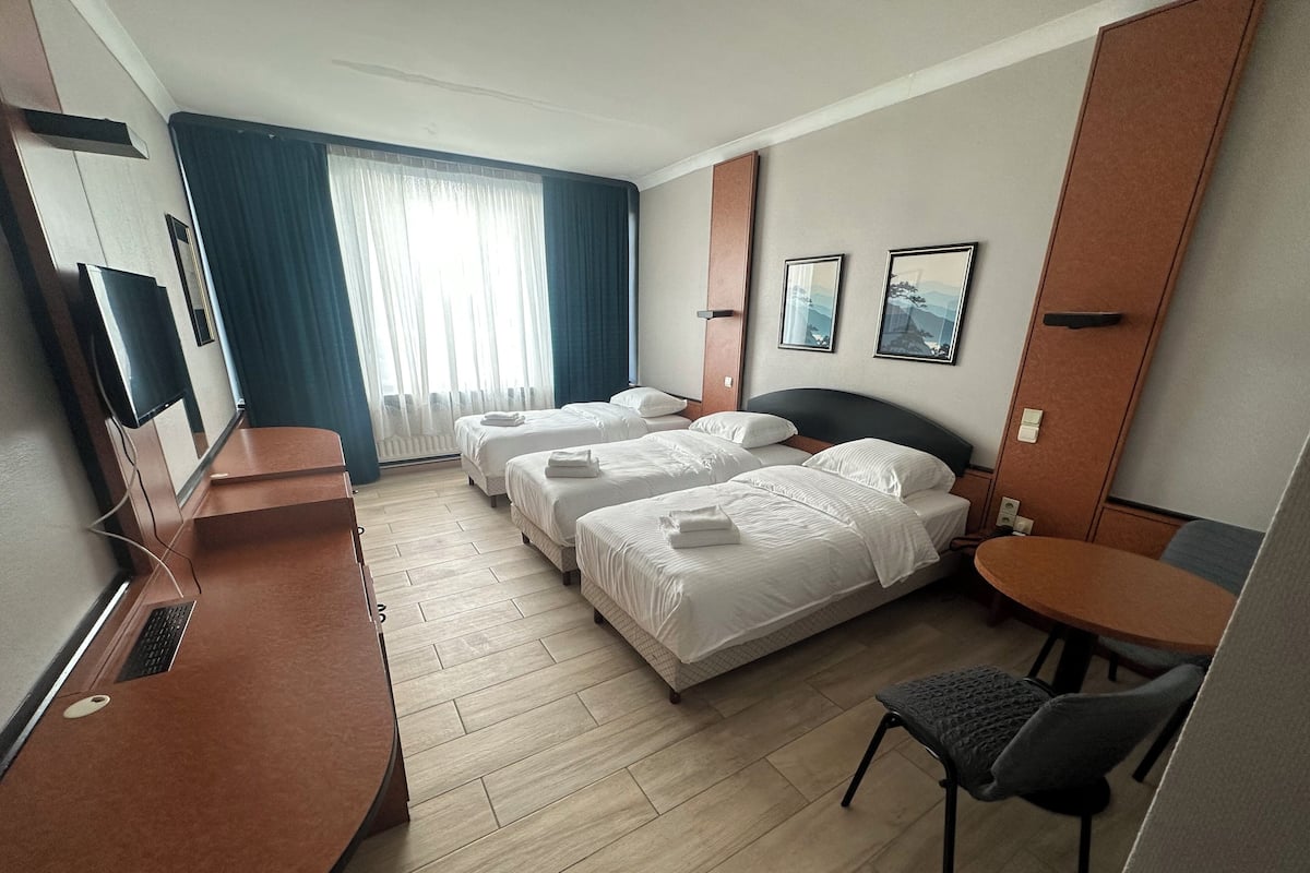 A hotel room with two beds, a desk, a chair, a small table, and a TV.
