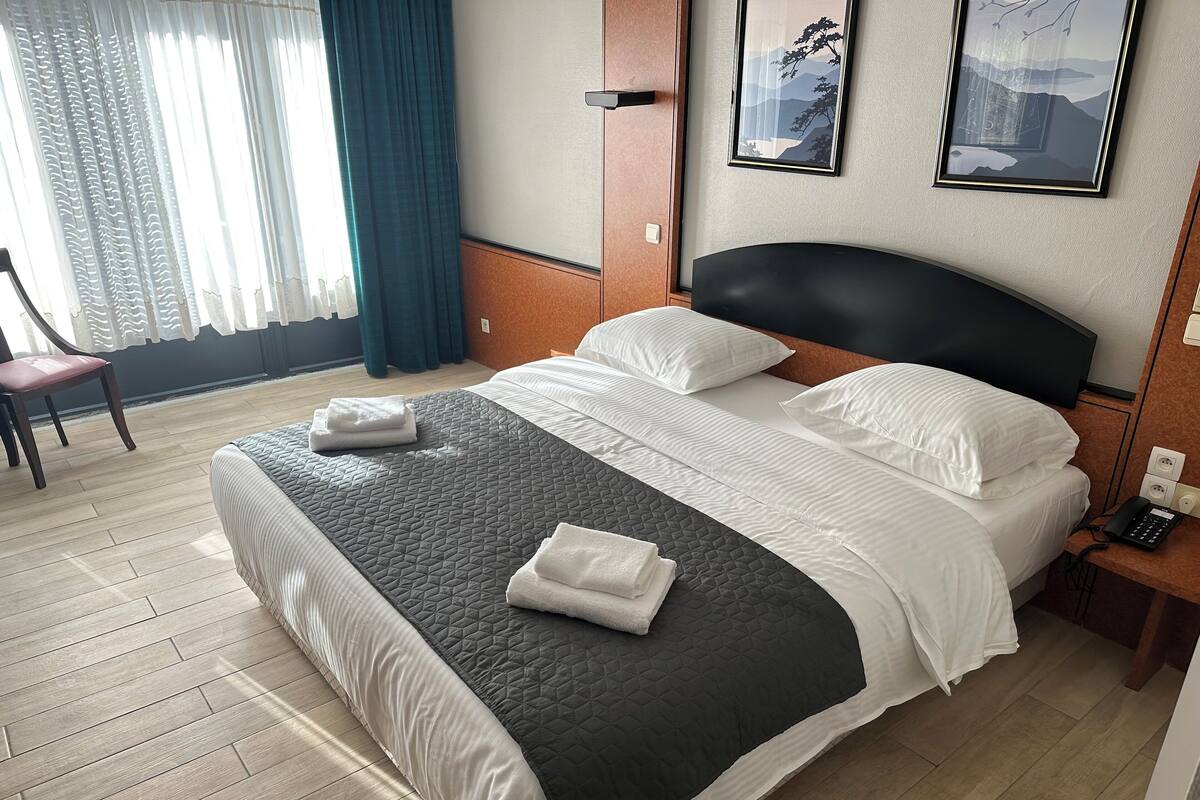 A neatly made bed with a black and white quilt, a wooden nightstand with a phone, and a framed picture on the wall.