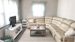 En stue med en beige hjørnesofa, et fladskærms-tv, et lille bord og en grøn kurv.