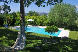 Ein Pool, umgeben von üppiger Vegetation und Bäumen, mit einer Hängematte und einem Sonnenschirm in der Nähe.
