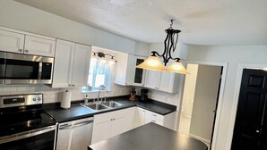 Una cocina moderna con electrodomésticos de acero inoxidable, armarios blancos y una isla central con taburetes.