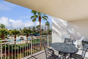 Relax on the balcony with a view of the resort pool surrounded by lush greenery and palm trees.