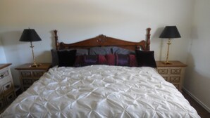 Een keurig opgemaakt bed met een witte deken, twee nachtkastjes met lampen, en een houten hoofdbord.
