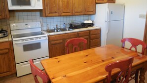 Een keuken met houten kasten, een magnetron, fornuis, spoelbak en een houten eettafel met stoelen.