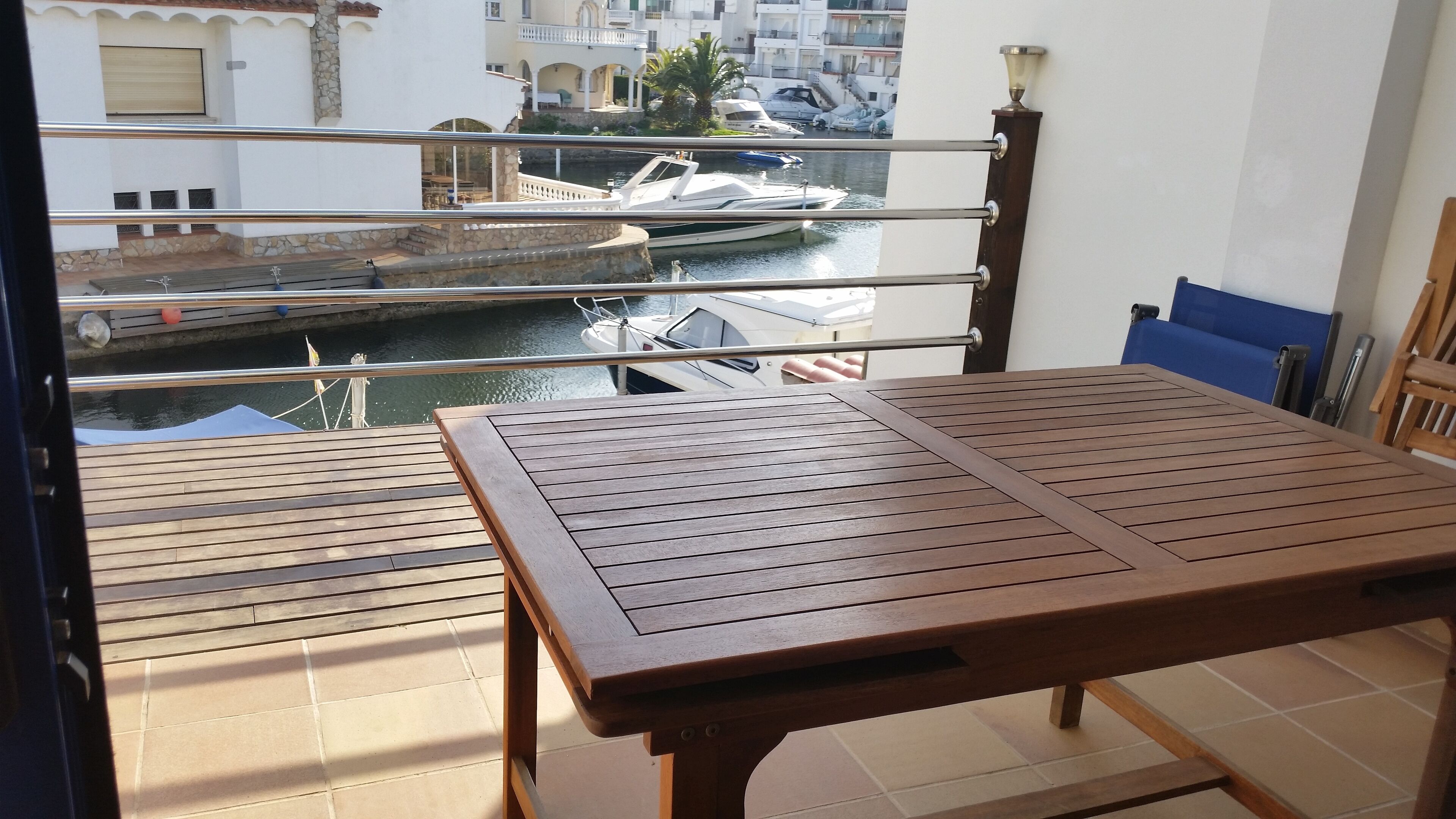 A balcony with a wooden table and chairs, overlooking a marina with boats.
