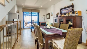 Un coin repas avec une table en bois et des chaises en osier, un téléviseur posé sur un meuble en bois, et un escalier menant à une autre pièce.