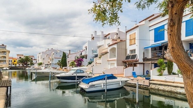 Un port de plaisance où sont amarrés des bateaux, entouré d’immeubles résidentiels dotés de balcons, avec un arbre au premier plan.