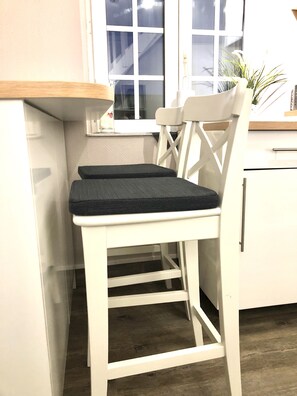 Una sedia di legno bianco con cuscino nero accanto a un bancone in cucina, vicino a una finestra.