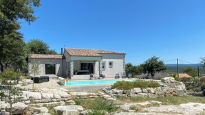 Une maison à deux étages avec une piscine, entourée de gros rochers et de verdure.