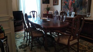 Een eetruimte met een ronde tafel, houten stoelen, een televisie en kunstwerken aan de wanden.