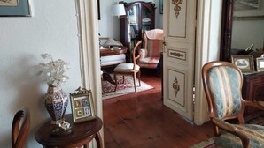 Een klassieke kamer met houten vloer, een tafeltje met vaas en fotolijst, een stoel en een kast met decoratieve details.
