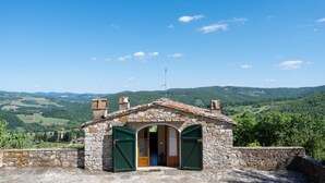 Un edificio in pietra con un piccolo ingresso, un camino e vista su dolci colline verdi.