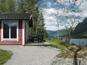 A small cabin with a porch, a table and chairs, and a view of a lake and mountains. - Holiday Home in Olden (Stryn)
