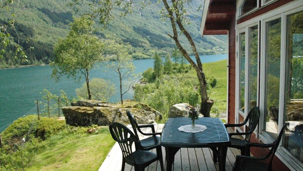 A deck with a table and chairs overlooking a lake and mountains. - Holiday Home in Olden (Stryn)