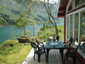 A deck with a table and chairs overlooking a lake and mountains.