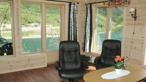 A room with two black leather chairs, a wooden table with a white doily, and a potted plant. Large windows offer a view of greenery and a body of water. - Holiday Home in Olden (Stryn)