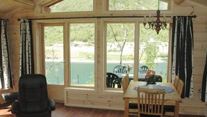 A dining area with a wooden table and chairs, large windows with a view of a body of water and greenery, and a chandelier hanging above. - Holiday Home in Olden (Stryn)