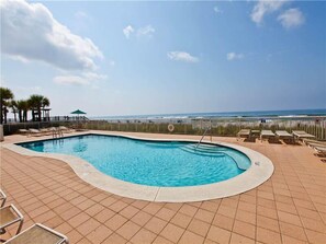 Relax by the pool surrounded by lounge chairs and umbrellas, with a clear view of the ocean.