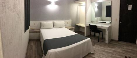 A hotel room with a bed, a desk, a chair, and a mirror.