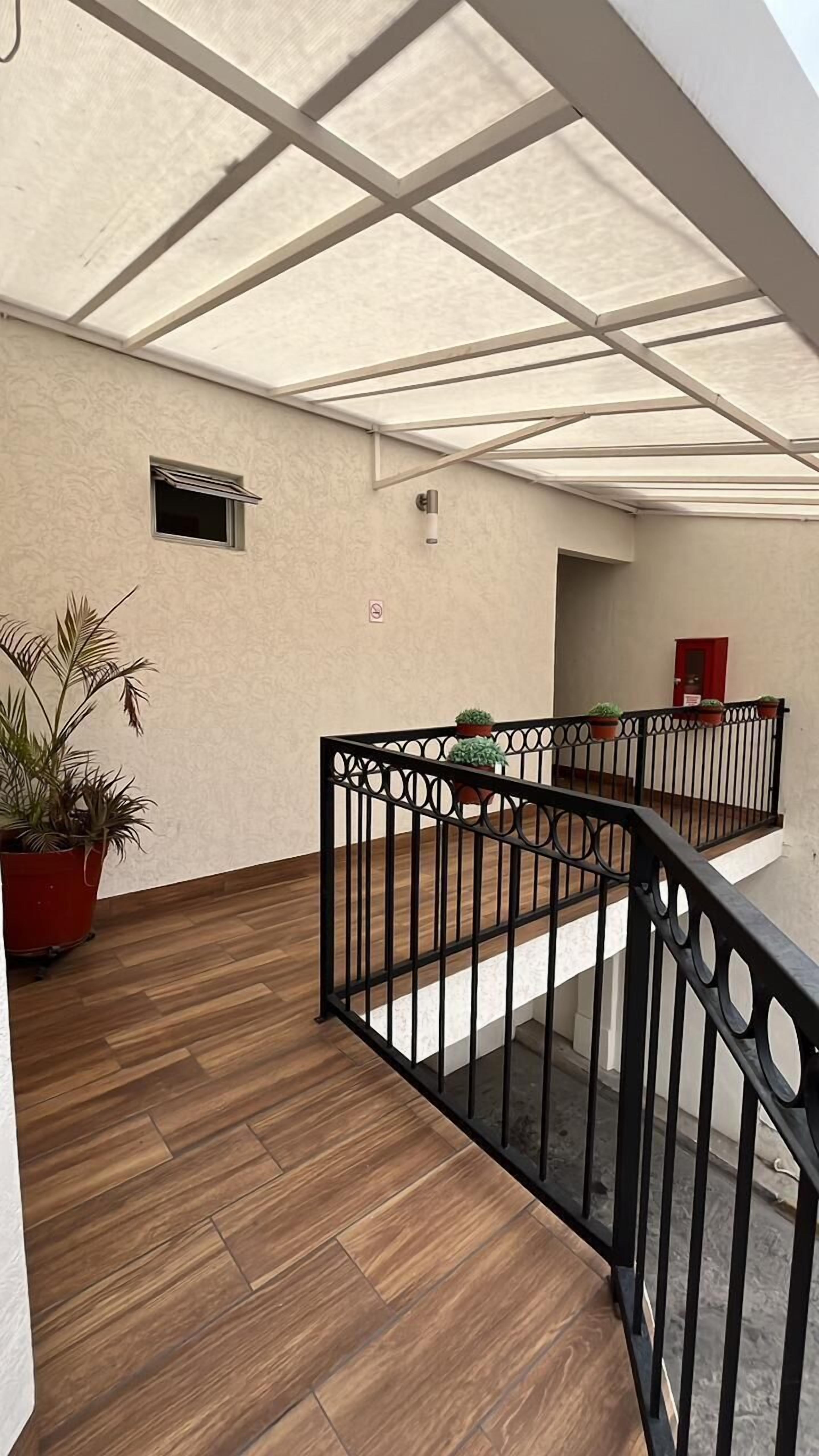 Un espace extérieur abrité doté d’un plancher en bois, d’une rambarde en métal et de plantes en pot.
