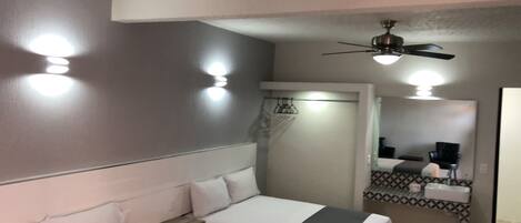 A hotel room with a bed, a ceiling fan, a mirror, and a bathroom with a sink and towel rack.