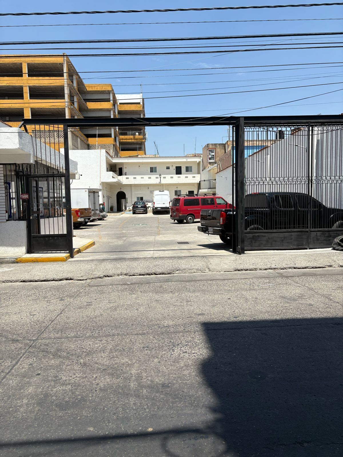 A parking lot with a gated entrance, a white building, and a red van parked inside.