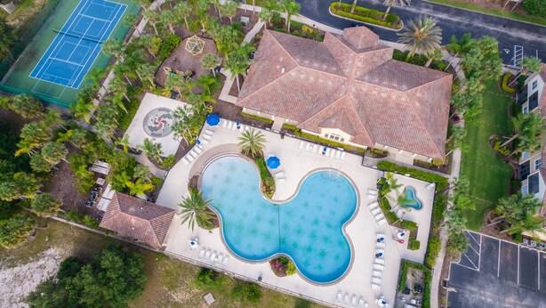 Vue aérienne d’un complexe hôtelier doté d’une piscine, d’un court de tennis et d’espaces paysagers.