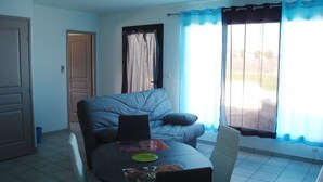 A dining area with a table and chairs, a sofa, and a window with curtains.