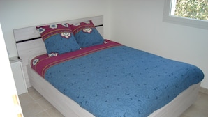A bed with a blue patterned bedspread and two pillows with a red and blue design.
