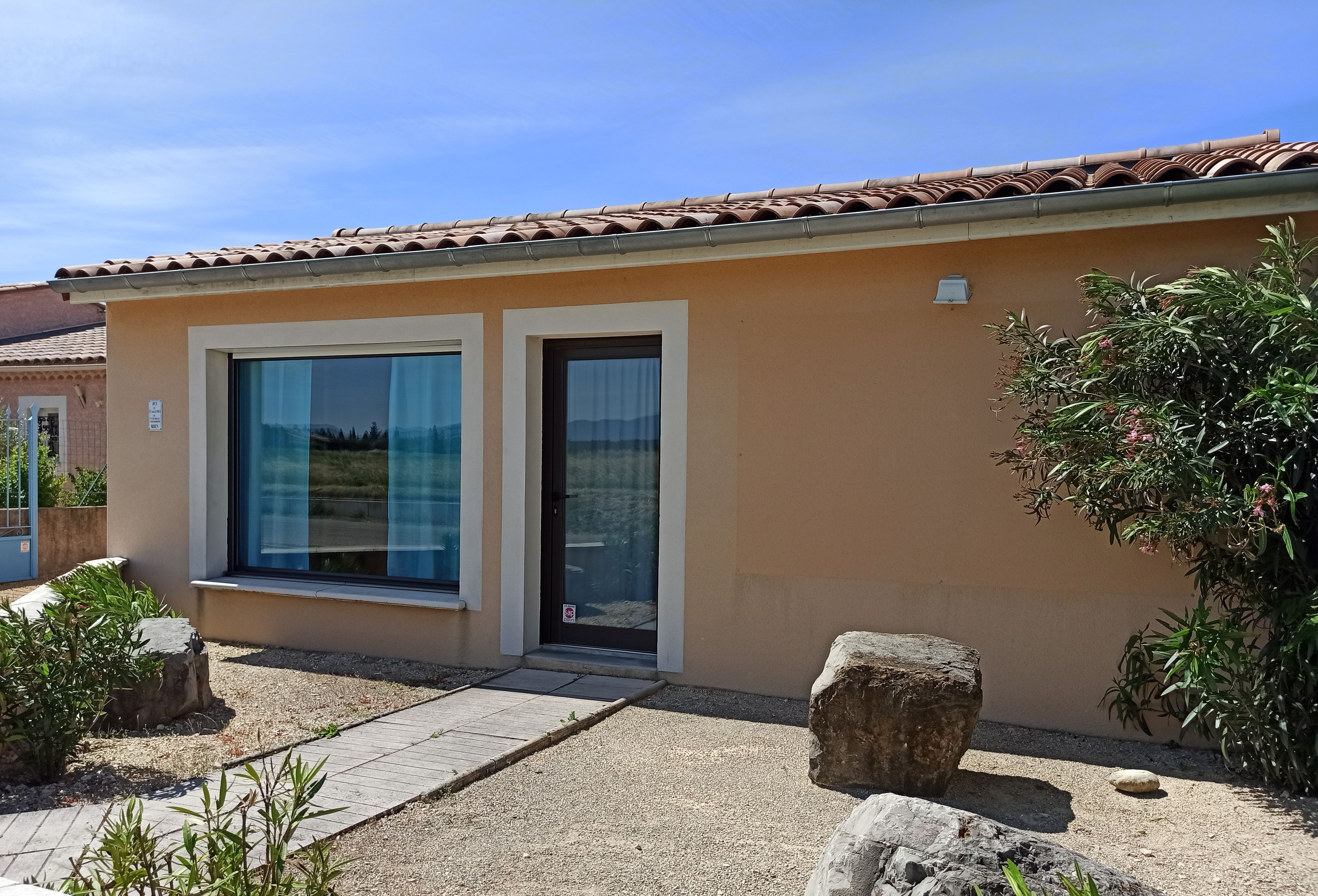 Un bâtiment moderne à la façade beige, doté de grandes fenêtres et d’un toit recouvert de tuiles.