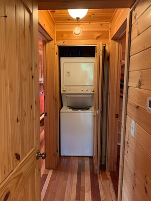 A narrow hallway with wooden walls and a ceiling light fixture. A white appliance, possibly a washer and dryer, is visible in the center. - Little T's Cabin Great Smoky Mtns, Hot Tub, Polar Express, King Bed, WiFi (Bryson City)