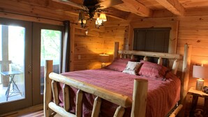Dormitorio de una cabaña de madera con cama, vigas de madera y una puerta corrediza de vidrio al exterior.