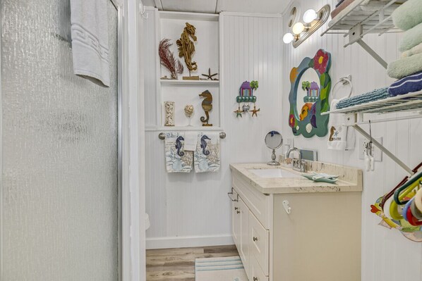 A bathroom with a vanity, shelves with decorative items, and a mirror.