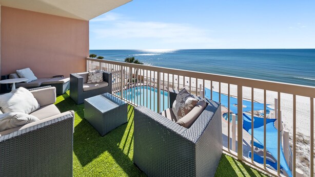 Un balcón con mobiliario de mimbre, una piscina y vista a la playa y el océano.