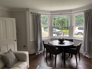 Una habitación de esquina con ventanal saliente, una mesa redonda con sillas, un sofá y un tazón sobre la mesa.