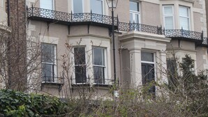 Un edificio de varios pisos con un ventanal de esquina, un balcón con barandilla de hierro forjado y una chimenea de ladrillo.