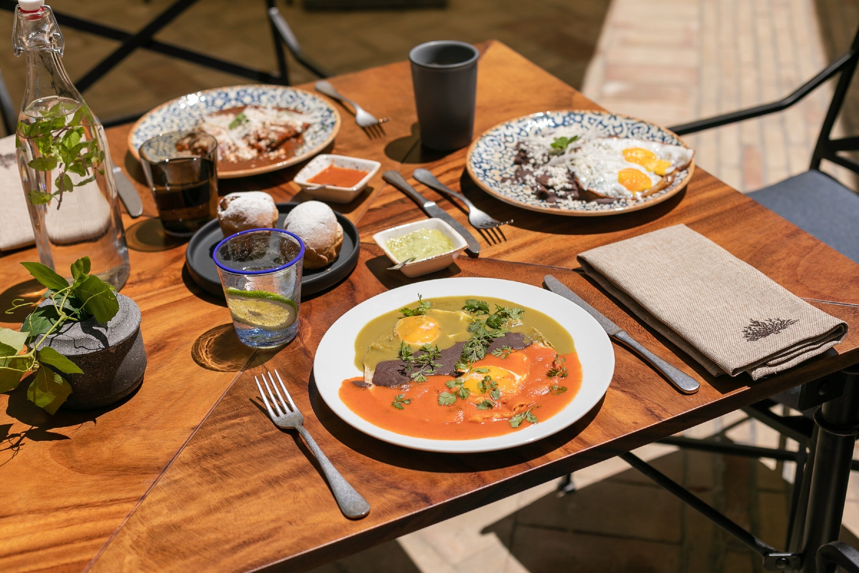 A wooden table with various dishes, including a plate of eggs, a bowl of soup, and a bottle of water.