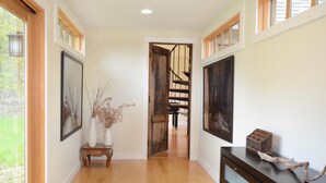 A hallway with wooden flooring, framed artwork on the walls, a small wooden bench, and a staircase leading to another level. - UNIQUE! 40 Pvt. Ac. Fireplace, Grill, Enclosed Heated Pool & Hot Tub (Saugerties)
