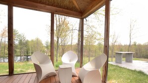 A covered outdoor area with modern white chairs and a small table, overlooking a natural landscape with trees and a body of water. - UNIQUE! 40 Pvt. Ac. Fireplace, Grill, Enclosed Heated Pool & Hot Tub (Saugerties)