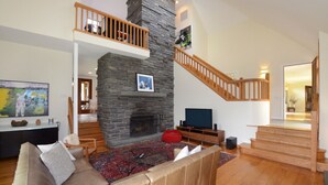 A spacious living room with a stone fireplace, a wooden staircase, and a comfortable seating area. - UNIQUE! 40 Pvt. Ac. Fireplace, Grill, Enclosed Heated Pool & Hot Tub (Saugerties)