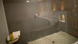 Et moderne badeværelse med et glasbadeværelsesafskærmning, et hvidt håndklæde og en shampoo på en stol.