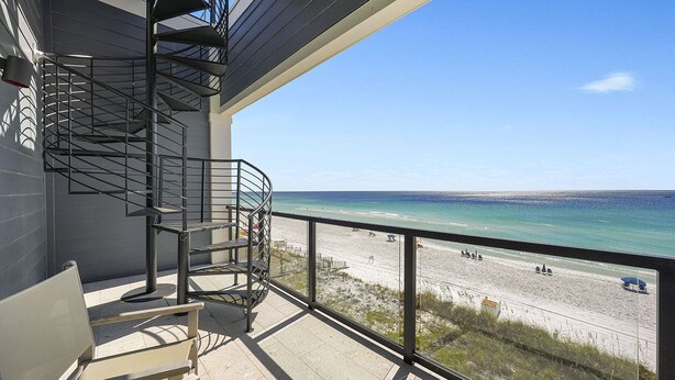A balcony with a spiral staircase, a beach view, and a chair.