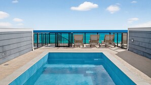 A rooftop pool with clear blue water, a view of the ocean, and several lounge chairs.