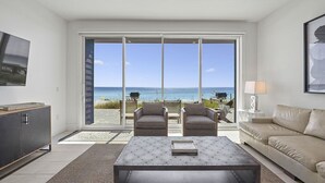 A modern living room with a large sliding glass door leading to a balcony with a view of the ocean.
