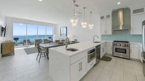 A modern kitchen with white cabinetry, a central island, stainless steel appliances, and a view to the ocean.