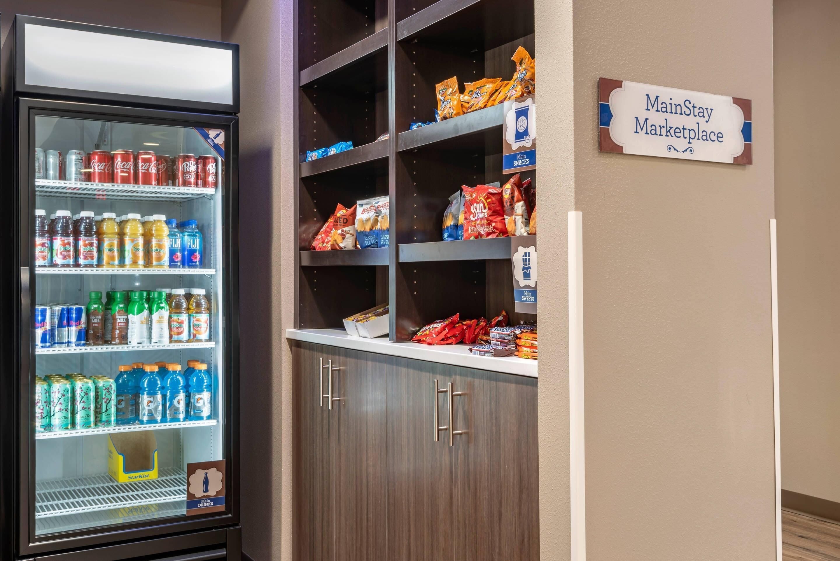 A vending machine stocked with beverages and snacks, a MainStay Marketplace sign, and a cabinet with snacks.