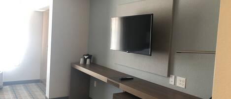 Habitación de hotel con televisión de pantalla plana montada en la pared, un banco de madera y un cubo de basura.