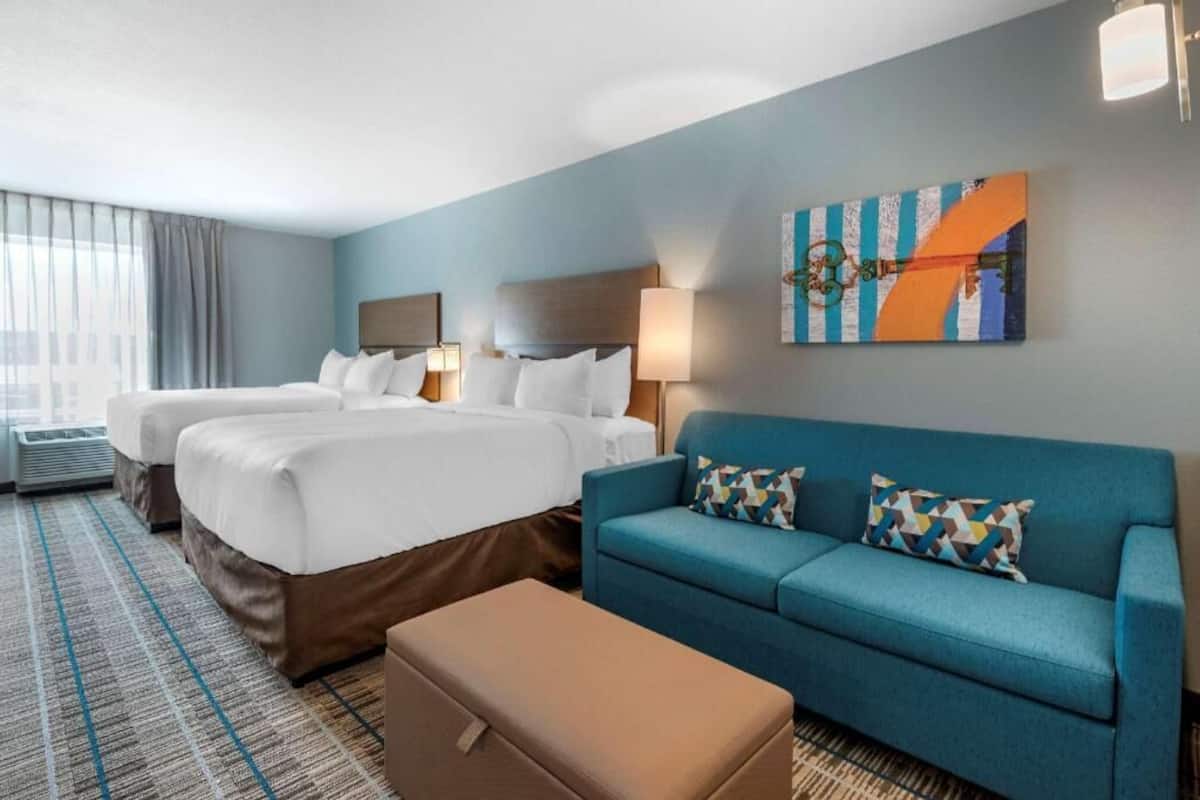 Ett hotellrum med två sängar, en soffa, ett konstverk som hänger på väggen och ett fönster med gardiner.