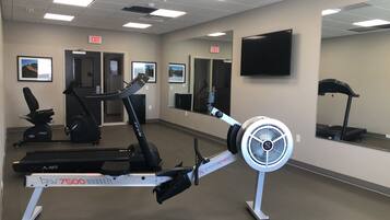A gym with cardio equipment, mirrors, and exit signs.